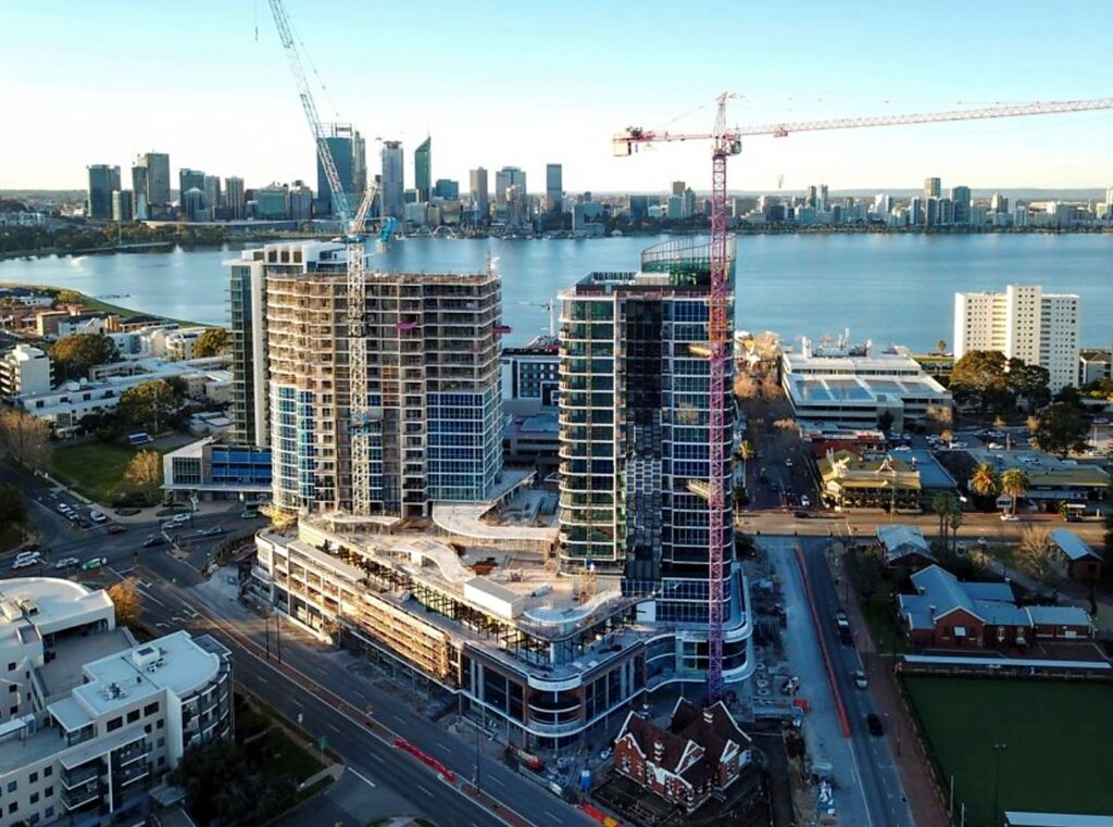 Aerial view of an active high-rise construction project with tower cranes and the Perth skyline and Swan River behind